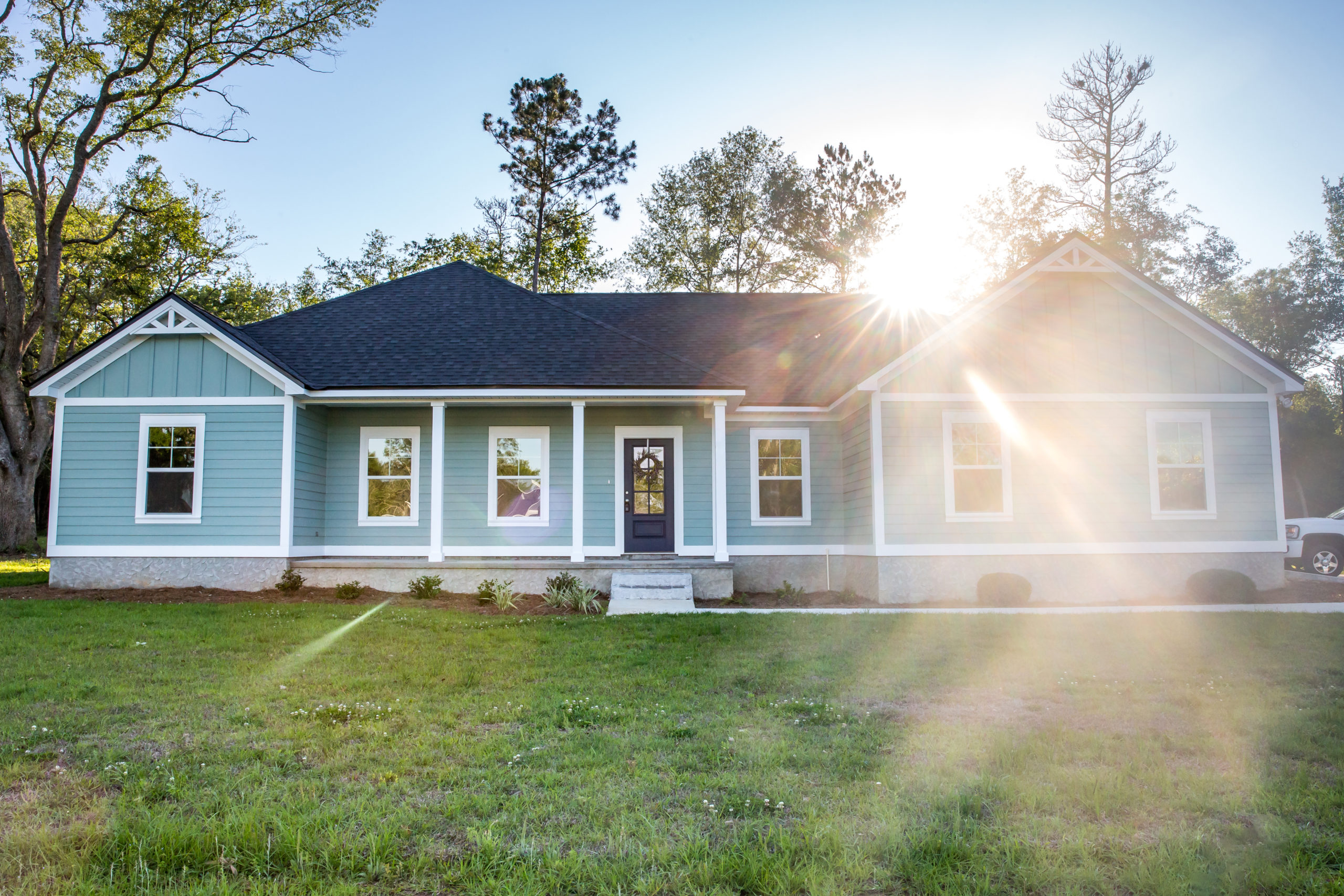 Front view of a brand new construction house with blue siding, a ranch style home with a yard and a sunflare